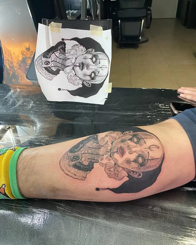 Muñeca arlequín en la pantorrilla, junto a su boceto en papel